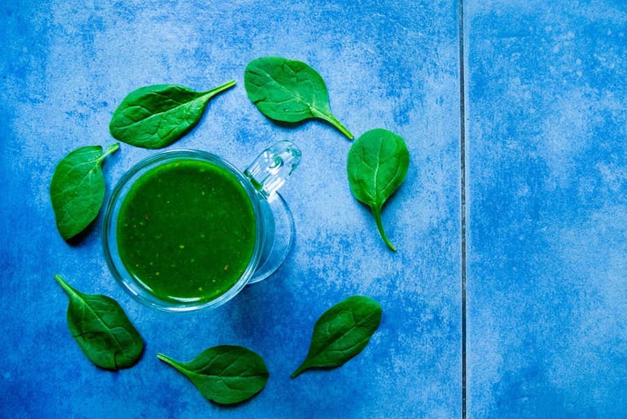Blaue Fliesen, auf denen ein grüner Smoothie, umringt von grünen Blättern, steht.